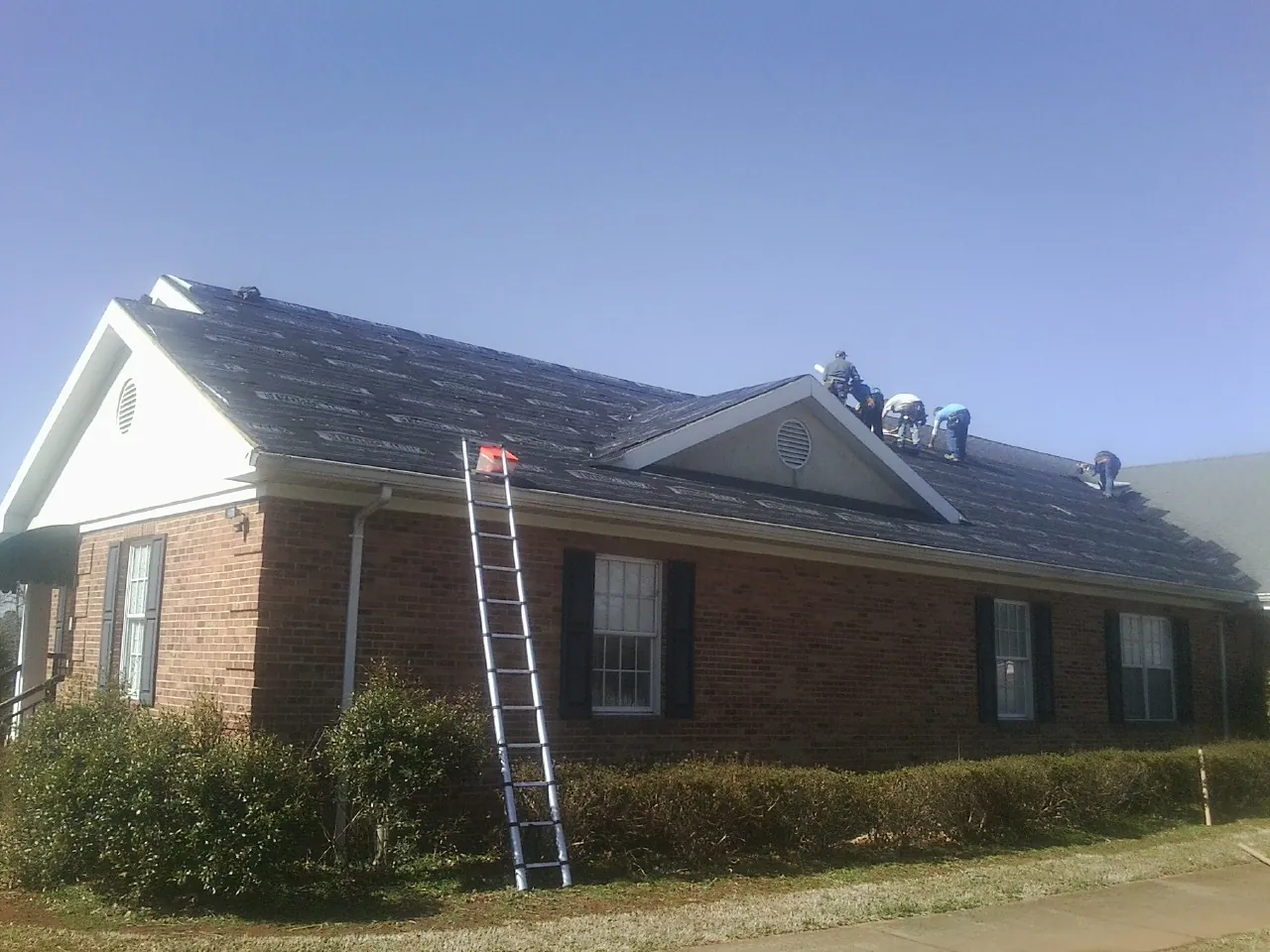Crew tearing shingles off a brick ranch roof with a ladder set — Emergency Roof Repair work by our crew in Courtenay