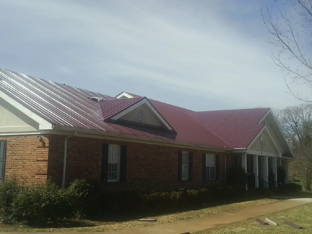 Red metal roof with gabled entries on a long brick building, from a Hail Damage Roof Repair job in Courtenay