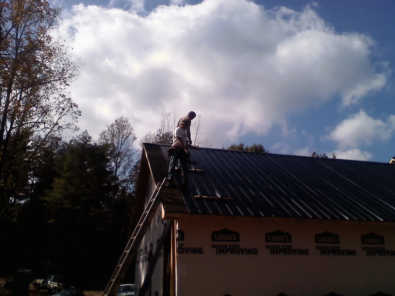 Roofer fastening dark metal panels high against a cloudy sky, from a Roof Inspection job in Courtenay