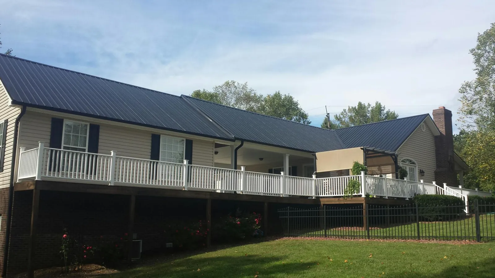 Black metal roof above a long white railed deck on a hillside home in Courtenay