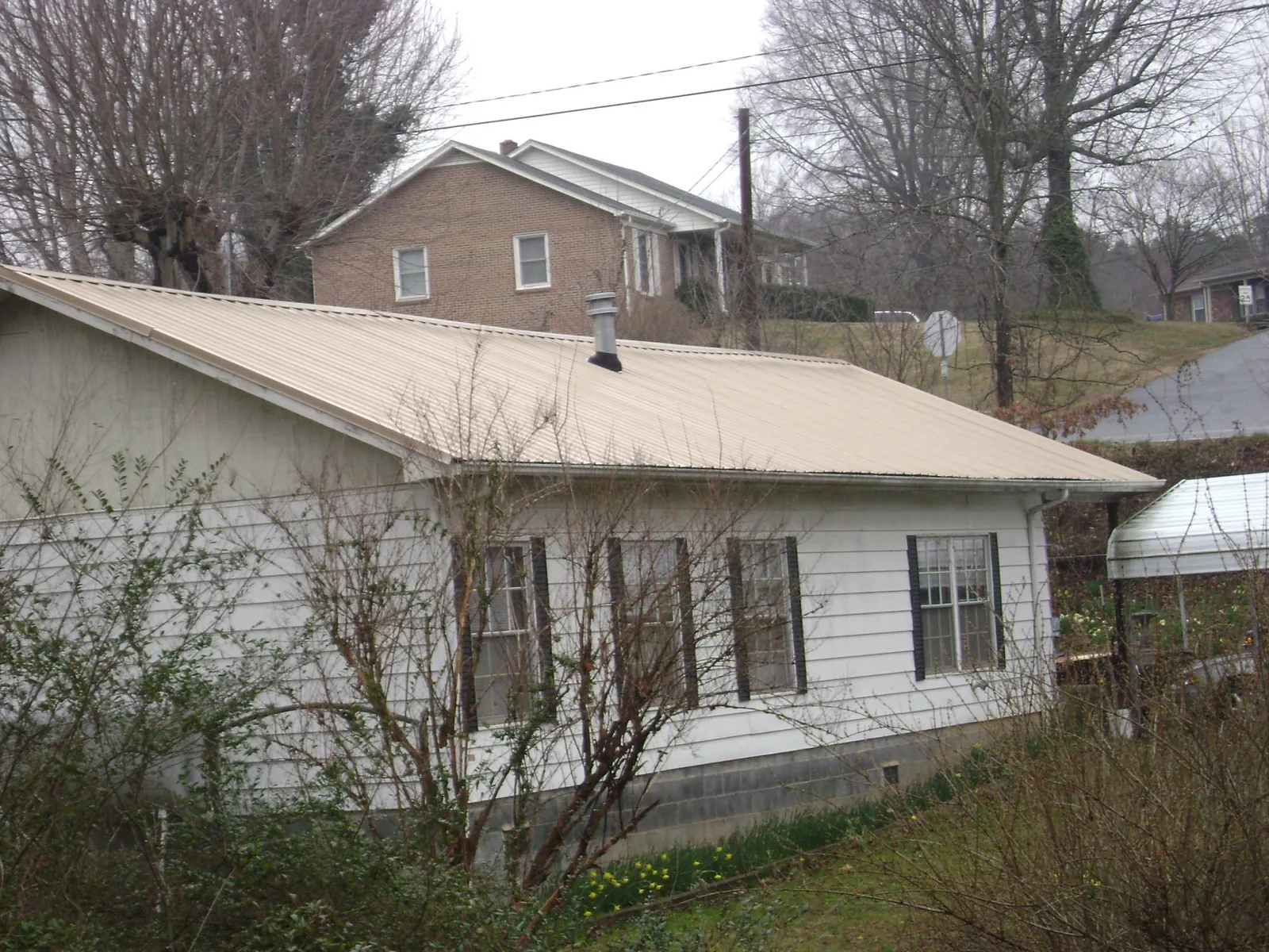Tan metal roof on a white sided house set into a hillside — Commercial Roofing by Roofing Brothers in Courtenay